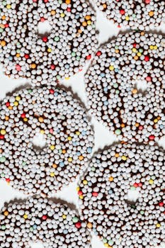 Top view of colorful chocolate-covered donuts with a sprinkle coating on a light backdrop.