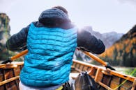 白天，一个穿蓝色夹克的人在群山环绕的宁静湖面上划船