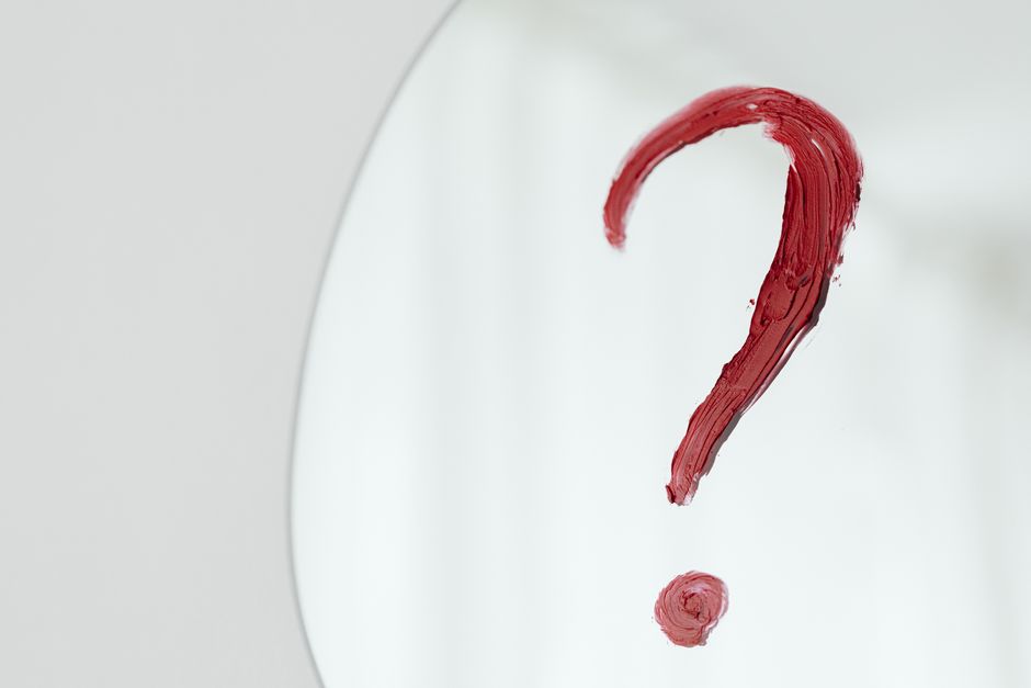 Close-up of a red question mark painted on a mirror with a white background.