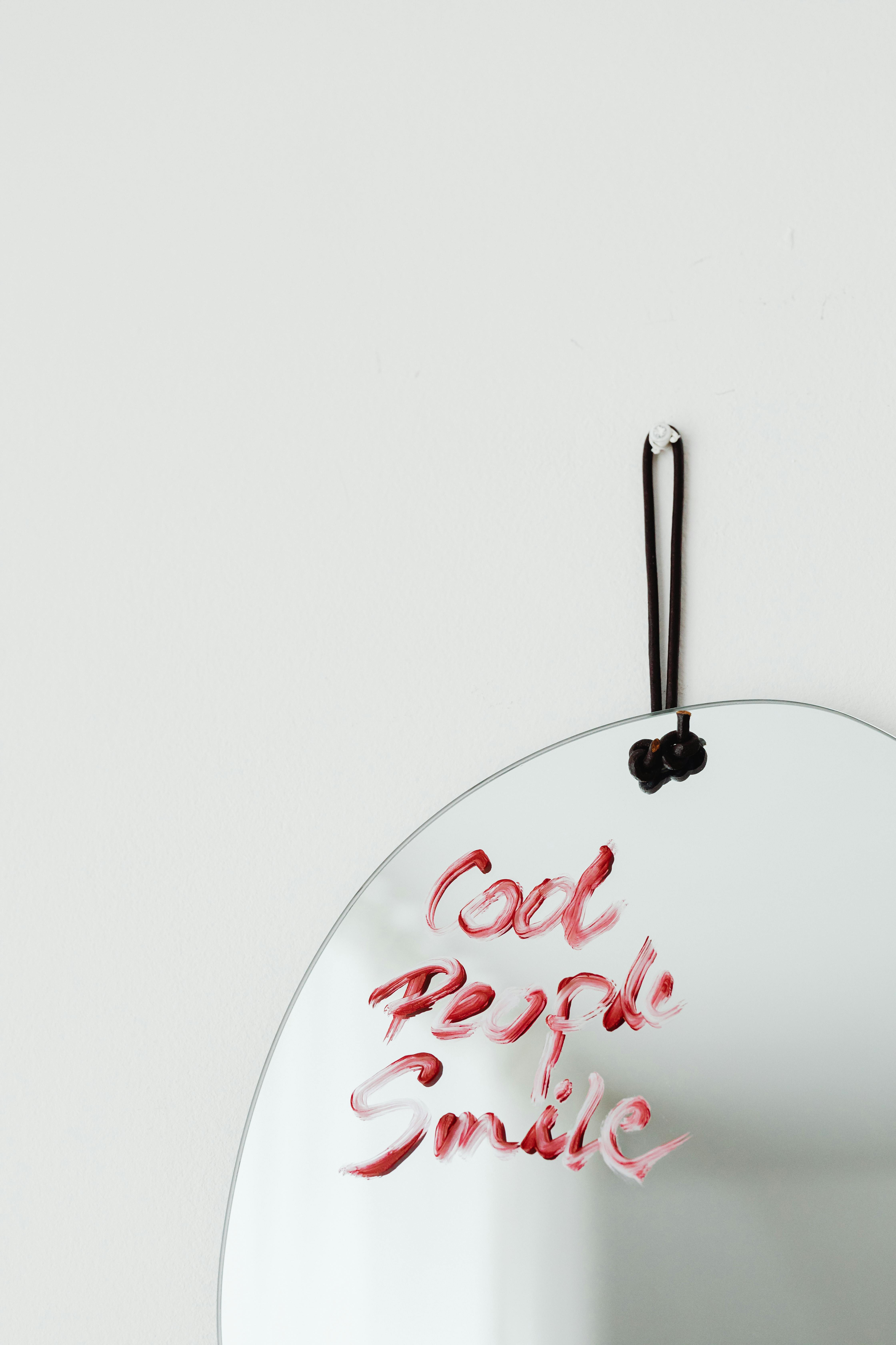 Elegant oval mirror with 'Cool People Smile' in red lipstick on a white background.