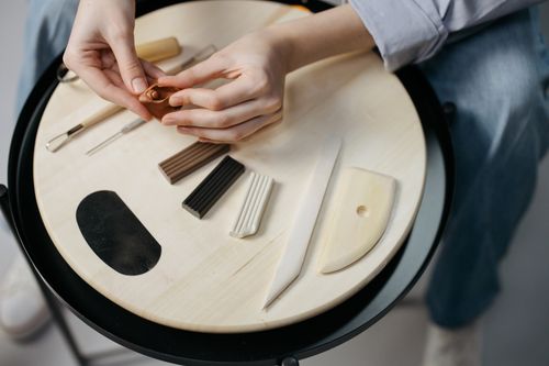 Hands shaping clay art with tools on a wooden bench — photo by cottonbro studio on Pexels