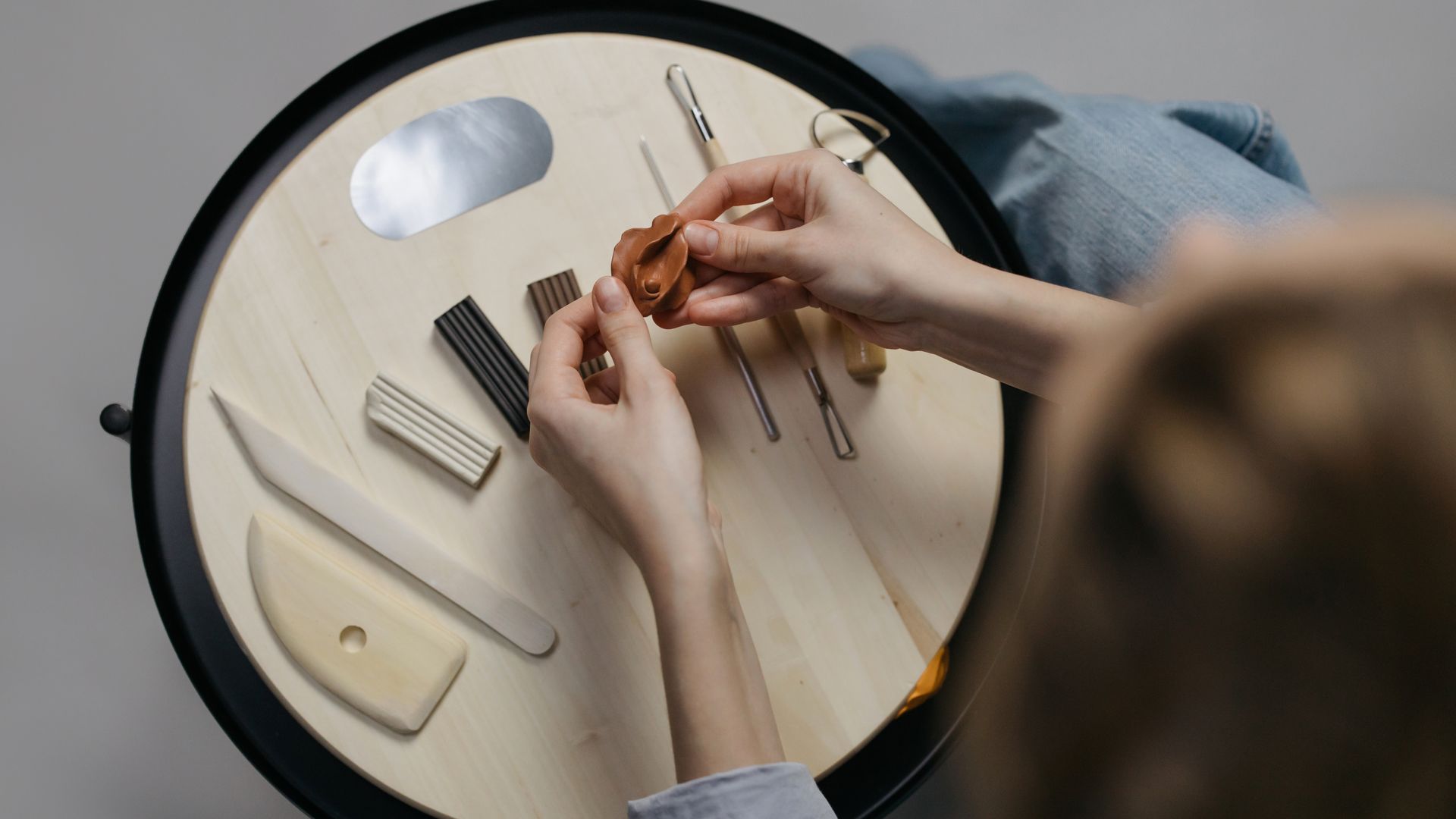 Hands modeling clay on a round table with tools, showcasing creativity in a workspace — top popular tools