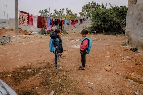 Side view of ethnic boy and girl talking in shabby yard with clothes hanging on rope