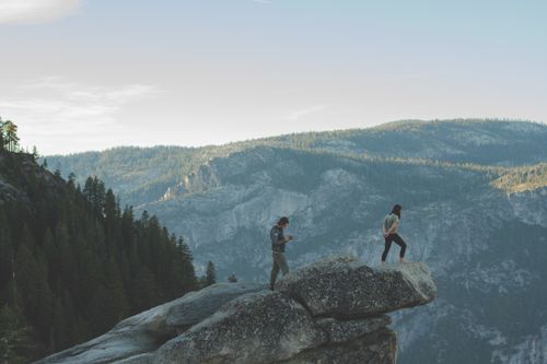 Free Two people standing on a cliff edge surrounded by stunning mountain scenery. Stock Photo