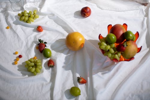 Ripe tasty fruits in glass vase and on white textile