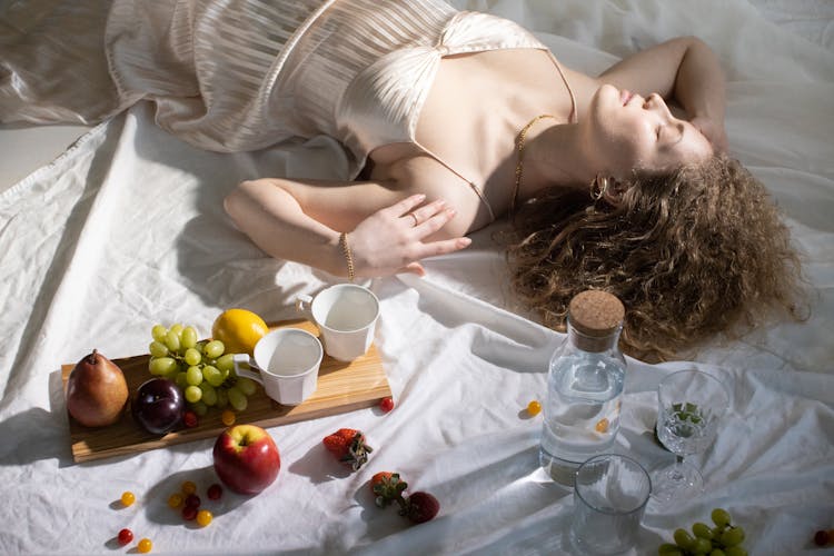 Young Woman In Trendy White Dress Near Cups And Fruits