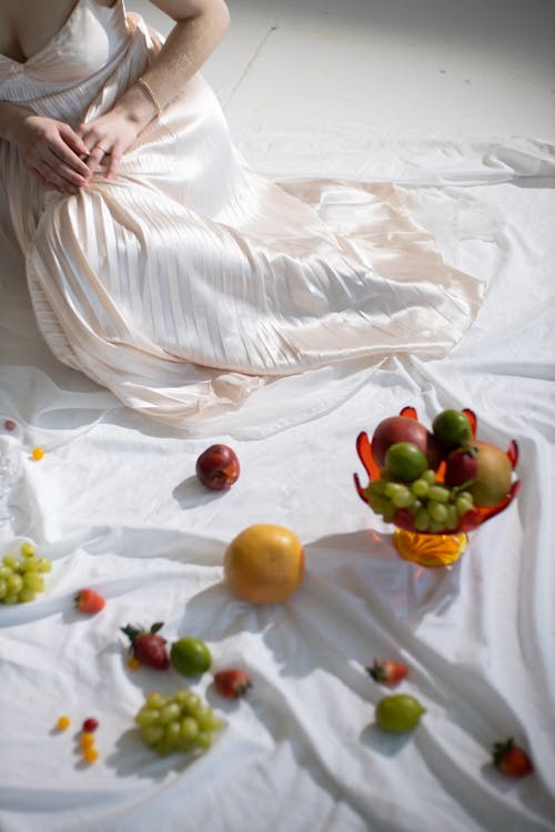 From above of crop anonymous female near geometrical vase with ripe fruits on white cloth with creases