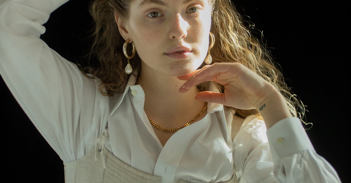 Young female touching long fair curly hair and looking at camera on black background
