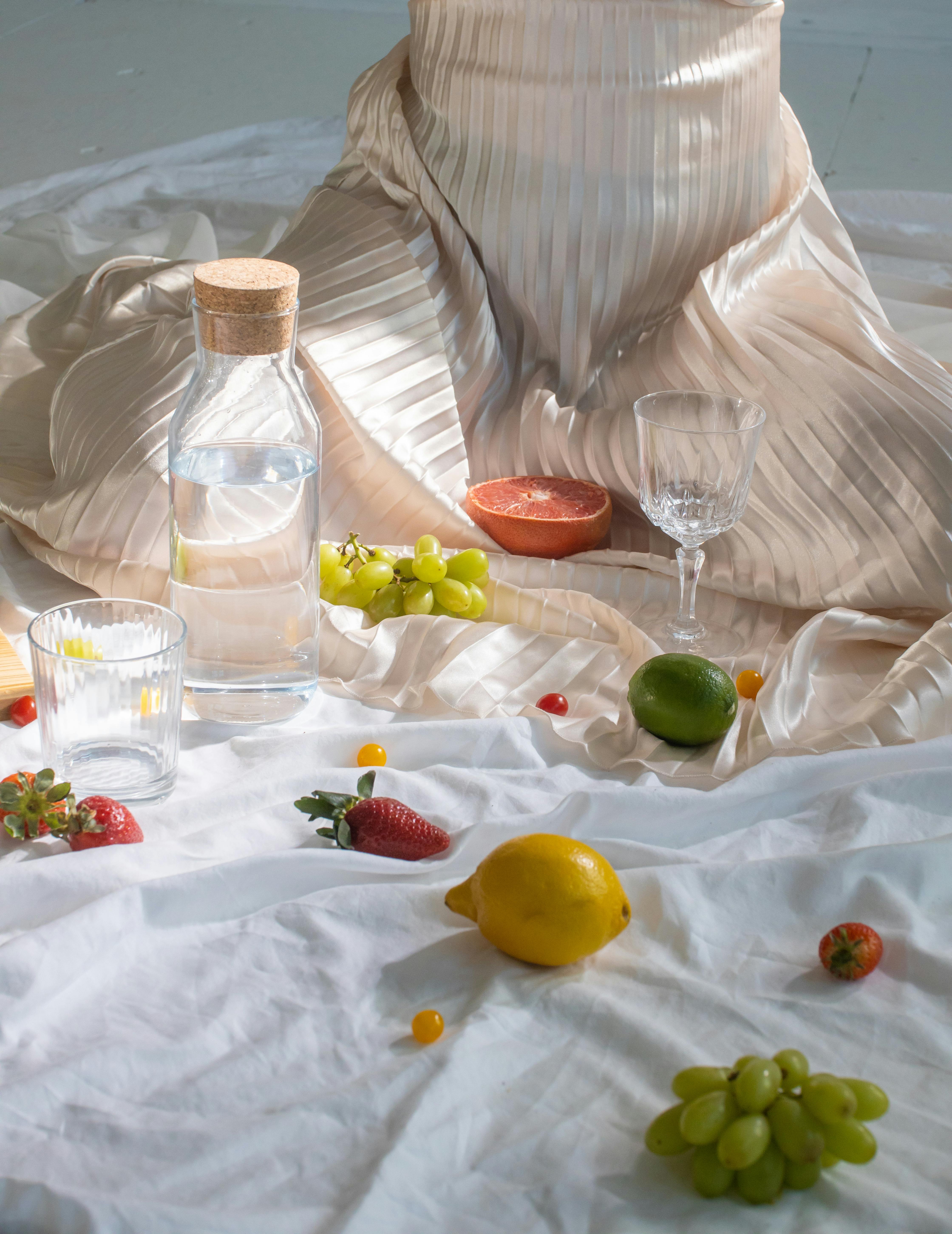 Free Crop anonymous female in white satin dress near chaotic citrus and berries on white fabric Stock Photo