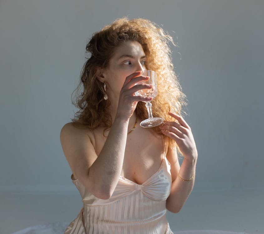 Free Young female with curly hair bare shoulders and chest looking away while drinking water on white background Stock Photo