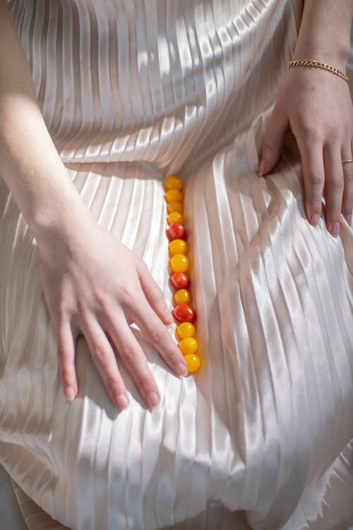 From above of crop unrecognizable female in romantic dress with ripe colorful berries resting on chair in sunlight