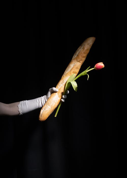 Crop woman showing flower and fresh baked baguette in black studio