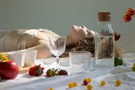 Peaceful young woman lying with closed eyes near assorted fruits on blanket