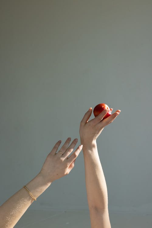 Crop faceless woman holding ripe apple in hand in light room