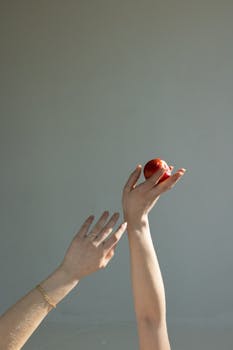 A minimalist composition of elegant hands holding a fresh apple against a gray background.