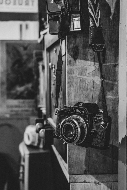 Black and white photo of a vintage Nikon film camera hanging indoors, with a nostalgic feel.