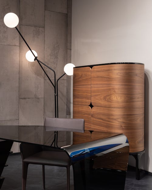 Empty table with chair placed near wooden cabinet at wall with creative glowing lamps inn modern workspace of stylish office