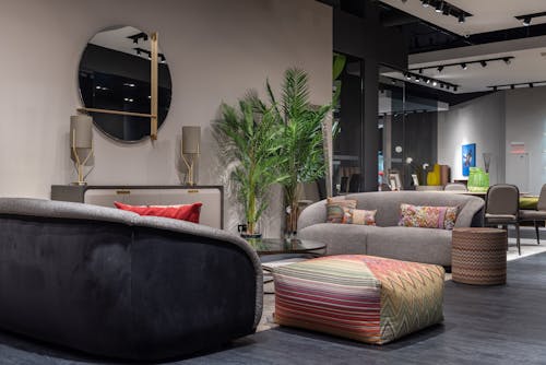 Interior of modern apartment with soft couches and colorful cushions and poufs placed near wall with mirror and decorations in modern apartment with green plants