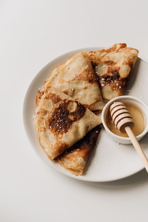 Free Appetizing crepes garnished with honey on a white plate, perfect for food photography. Stock Photo