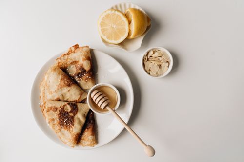Free Top view of delicious crêpes with honey dipper, sliced lemon, and almonds. Stock Photo