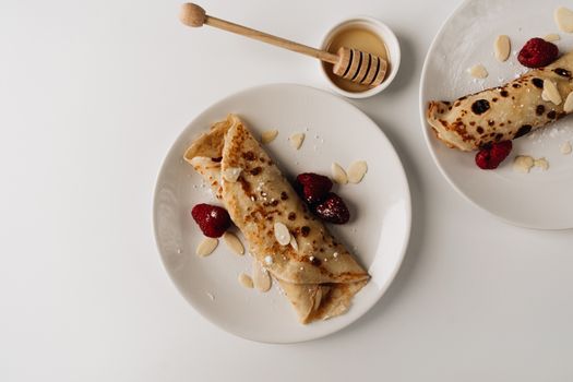 Scrumptious pancakes rolled with almonds, raspberries, and honey drizzle on a white plate.