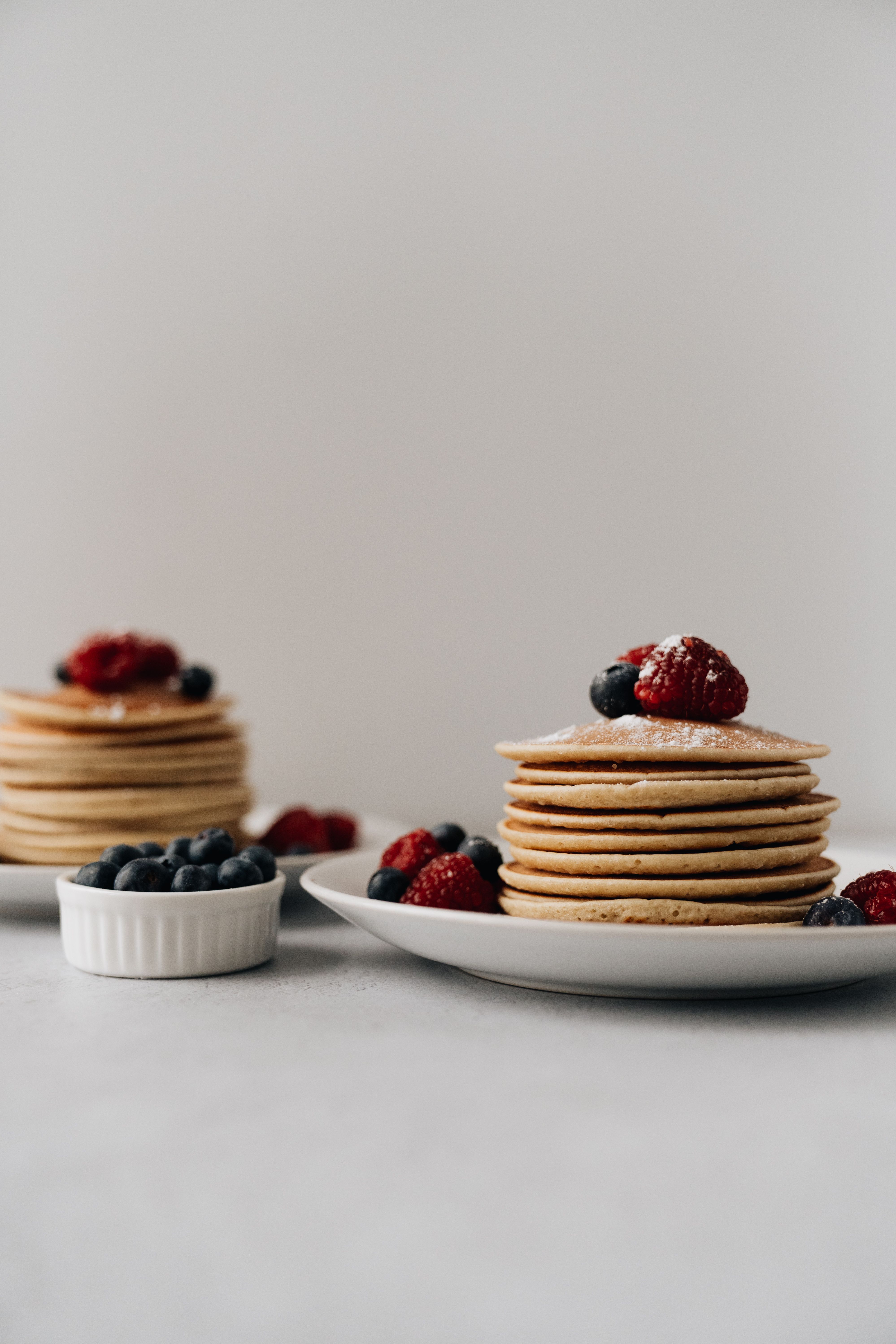 Stacks of pancakes with blueberries and raspberries on a white surface, creating a tempting food scene.