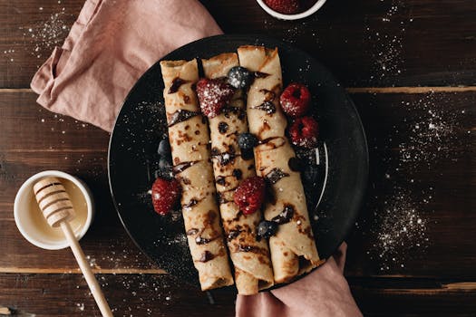Top view of rolled crepes with berries and honey on a dark plate, deliciously styled.