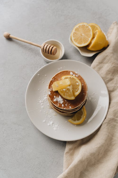 A Stack of Pancakes on a Ceramic Plate with Honey Dipper on the Side