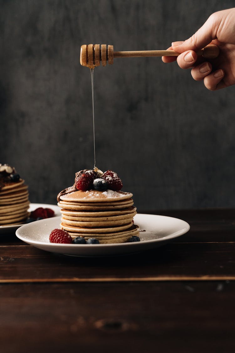 A Person Pouring Honey On Pancakes