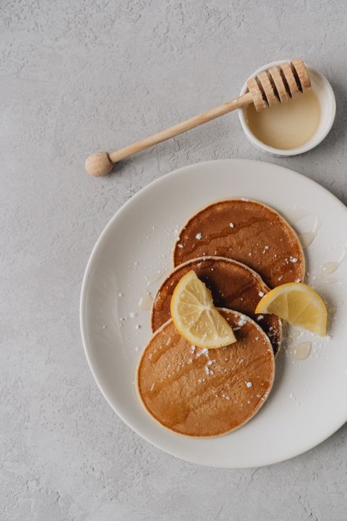 Free Delicious pancakes topped with lemon slices and honey on a white plate in a flat lay composition. Stock Photo