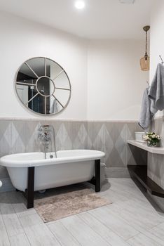 Interior of modern comfortable illuminated bathroom with round shaped mirror and beige walls