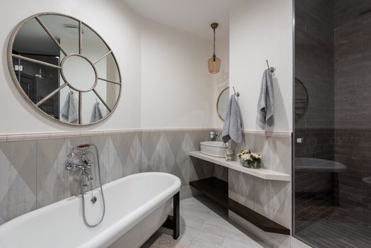 Interior of contemporary bathroom with clean white bathtub placed under stylish round mirror on light walls