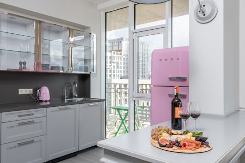 Plate with fresh delicious fruits placed near bottle of red wine on light table in stylish kitchen in daylight