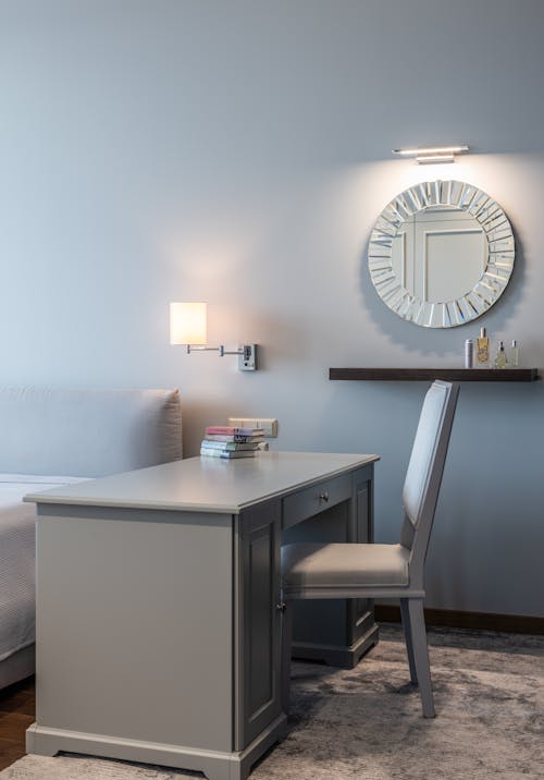 Table with stack of books placed against wall with round mirror in light modern room in apartment