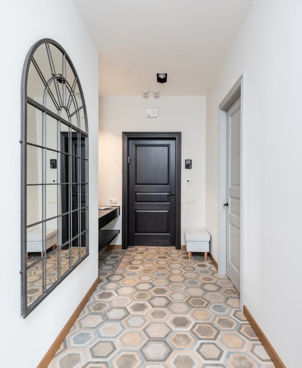 Interior of spacious corridor with colorful tile floor and decorative mirror hanging on light wall placed in contemporary apartment