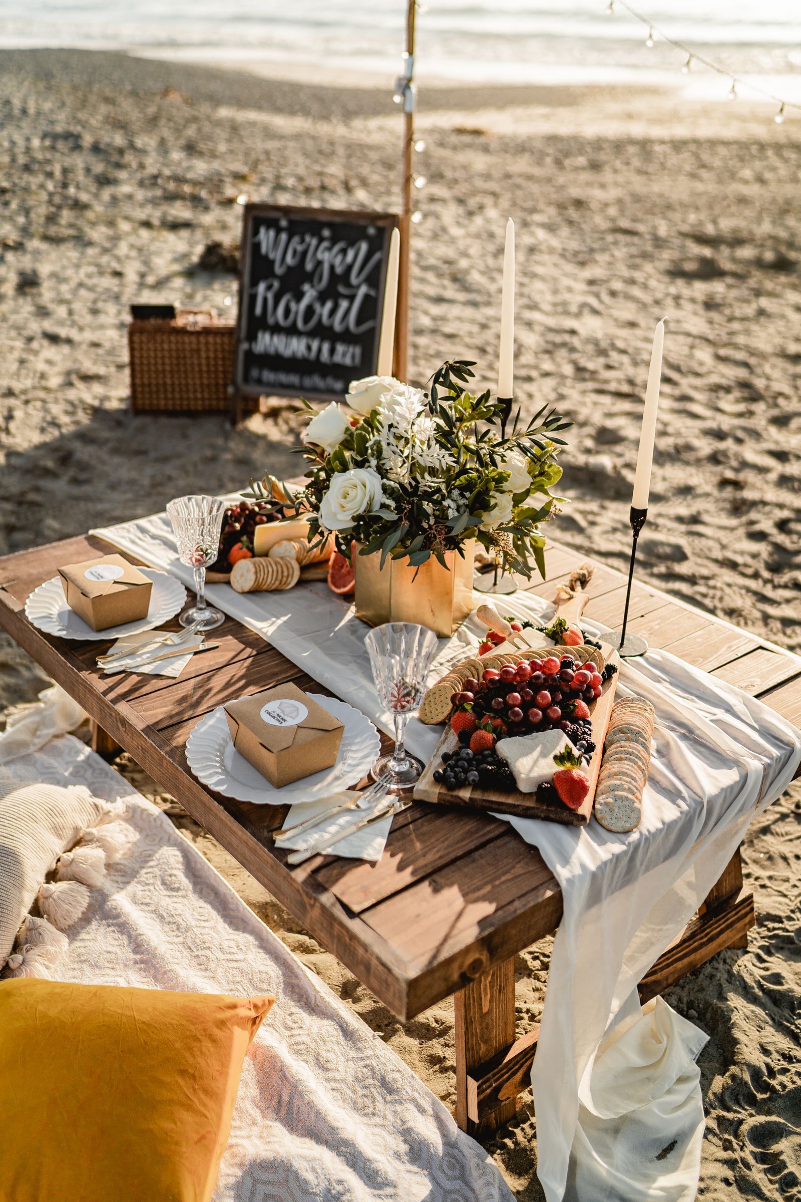 Beach picnic table with charcuterie and floral decor by the sea