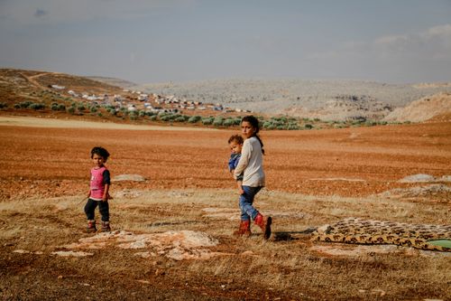 Free Full body of ethnic poor children walking in rustic field with hills under gloomy sky Stock Photo