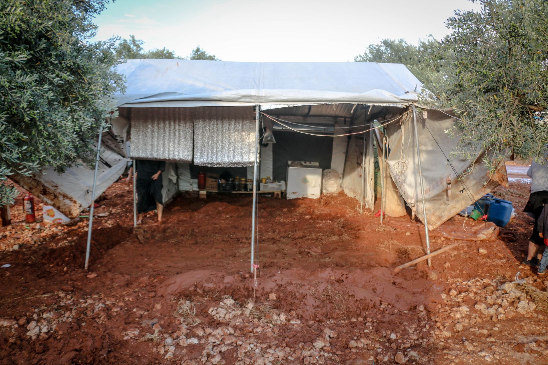 White weathered camping tent with canopy and personal belongings located on ground near green trees in rural area of countryside