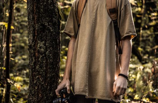 A young man with a camera and backpack exploring a lush forest setting, captured in Portland.
