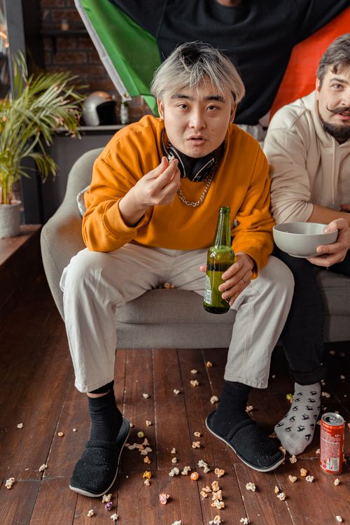 Free Two friends enjoying snacks and drinks indoors during a casual gathering. Stock Photo