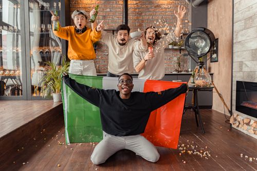 Free Four friends celebrate indoors with popcorn and flags, enjoying a leisure moment. Stock Photo