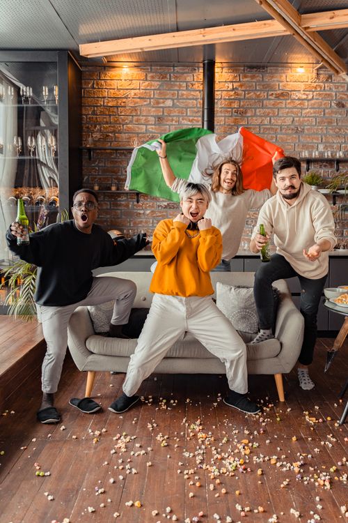 Free Diverse group of friends celebrating indoors with drinks and an Italian flag. Stock Photo