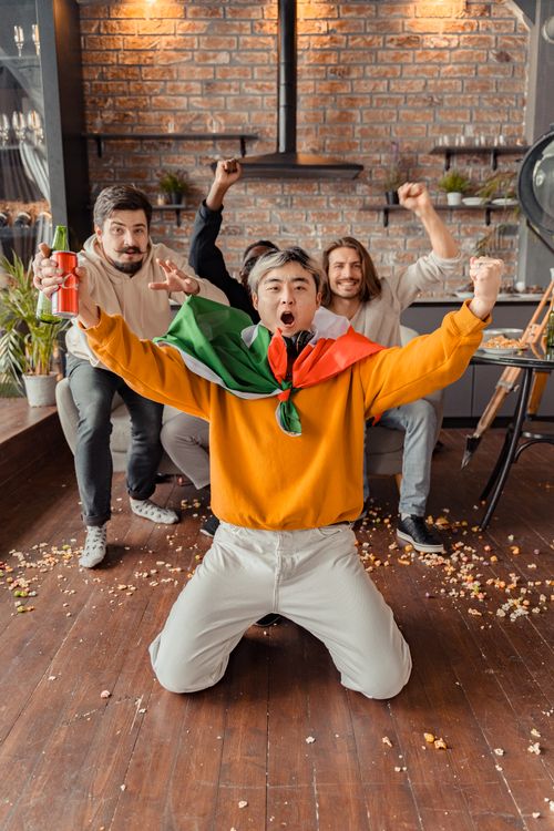 Free Group of friends cheering indoors, filled with excitement and energy, supporting their team. Stock Photo