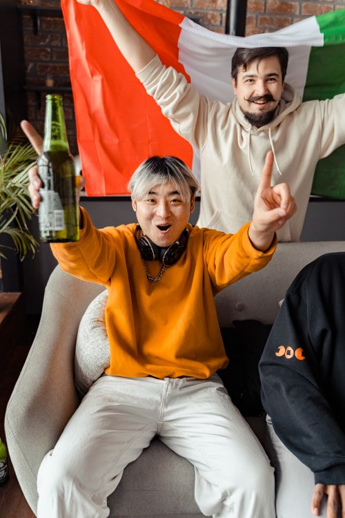 Free Two friends celebrating with flags and drinks. Energetic atmosphere indoors. Stock Photo