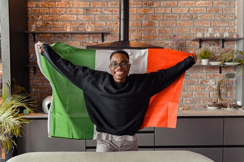 Free Cheerful man holding Italian flag indoors, celebrating with a smile. Stock Photo