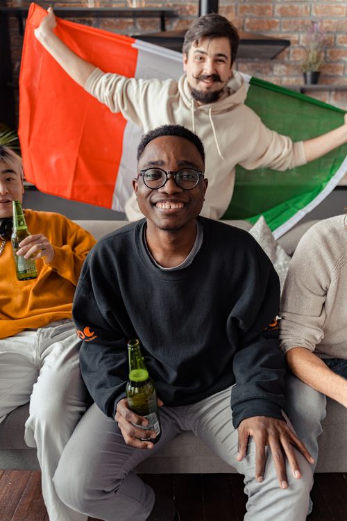 Free Group of diverse friends cheering and celebrating indoors with beers and a flag. Stock Photo