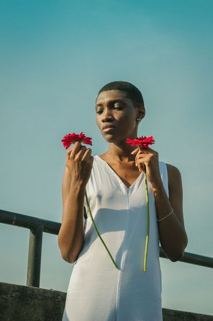 A stylish, serene portrait of a woman in white holding red flowers, set outdoors in daylight.