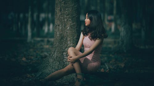 Селективная фотография женщины в розовом платье, сидящей на корнях деревьев