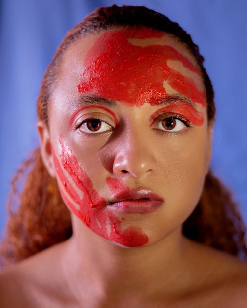 Free Striking portrait of a woman with vivid red face paint, emphasizing artistic expression. Stock Photo