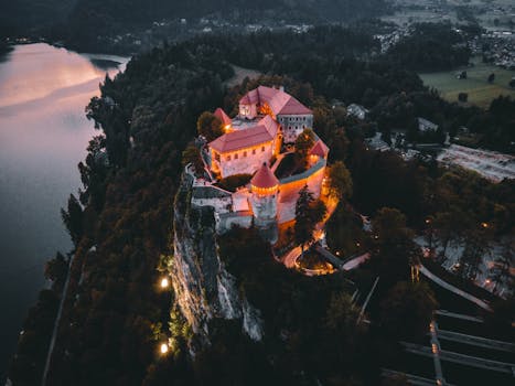 Stunning aerial photo of a historic castle illuminated at twilight, surrounded by nature.